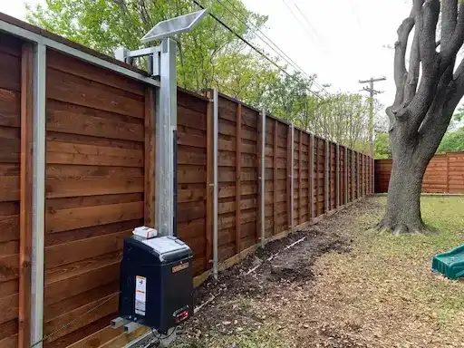 Solar-powered automatic gate operator installed beside a cedar fence