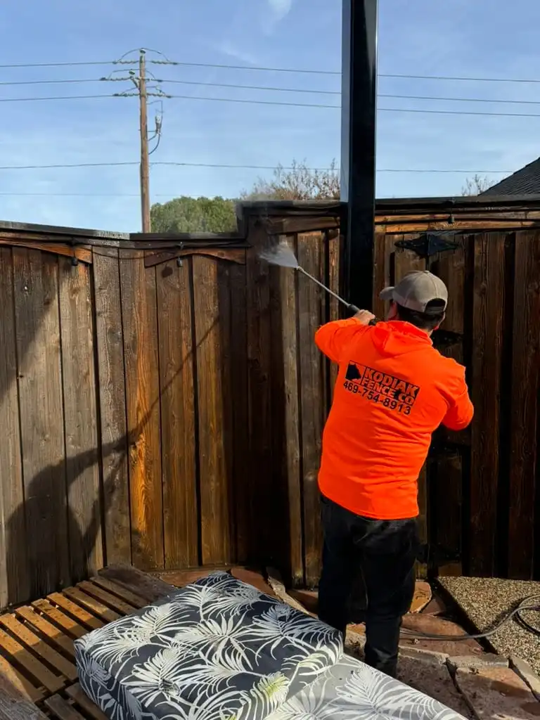 Kodiak crew member pressure washing a weathered cedar fence before staining